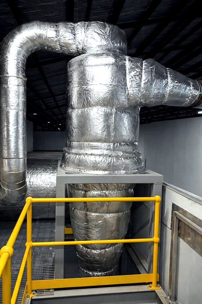 Large silver-wrapped industrial process housing and ducting system in a warehouse environment